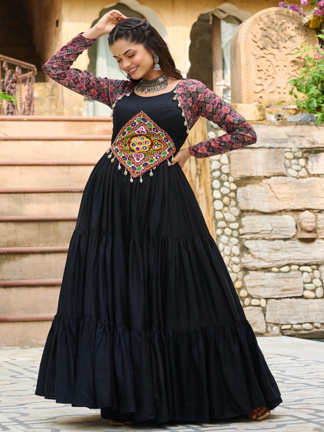 Woman in a black dress with floral sleeves and a colorful belt standing outdoors.
