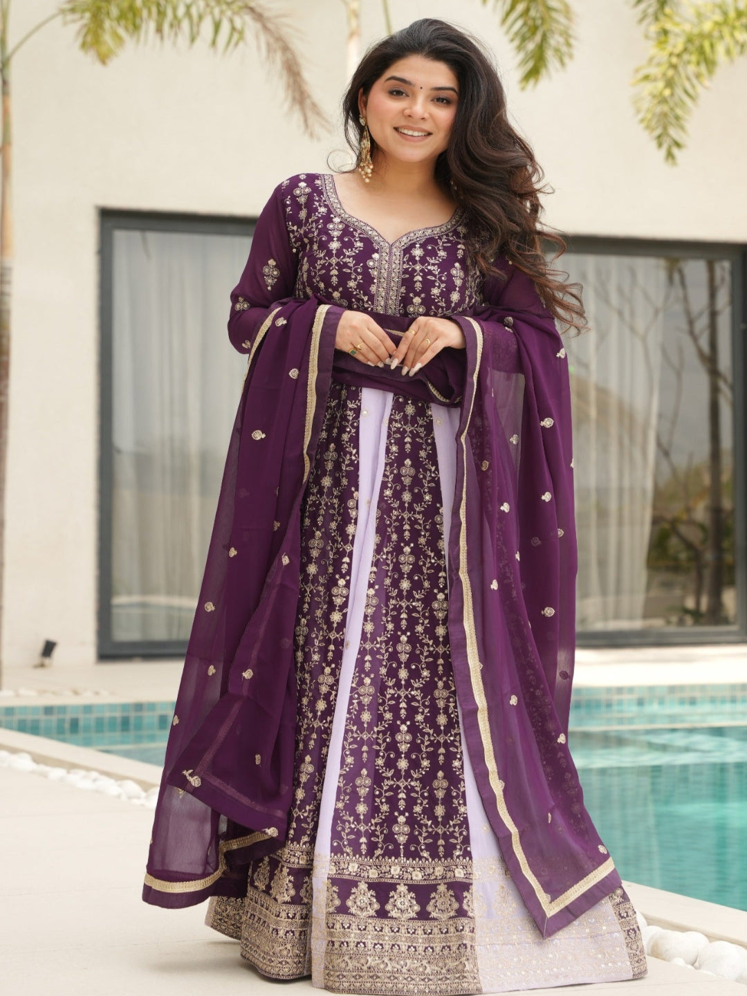 Woman in a purple traditional outfit standing by a pool with greenery in the background