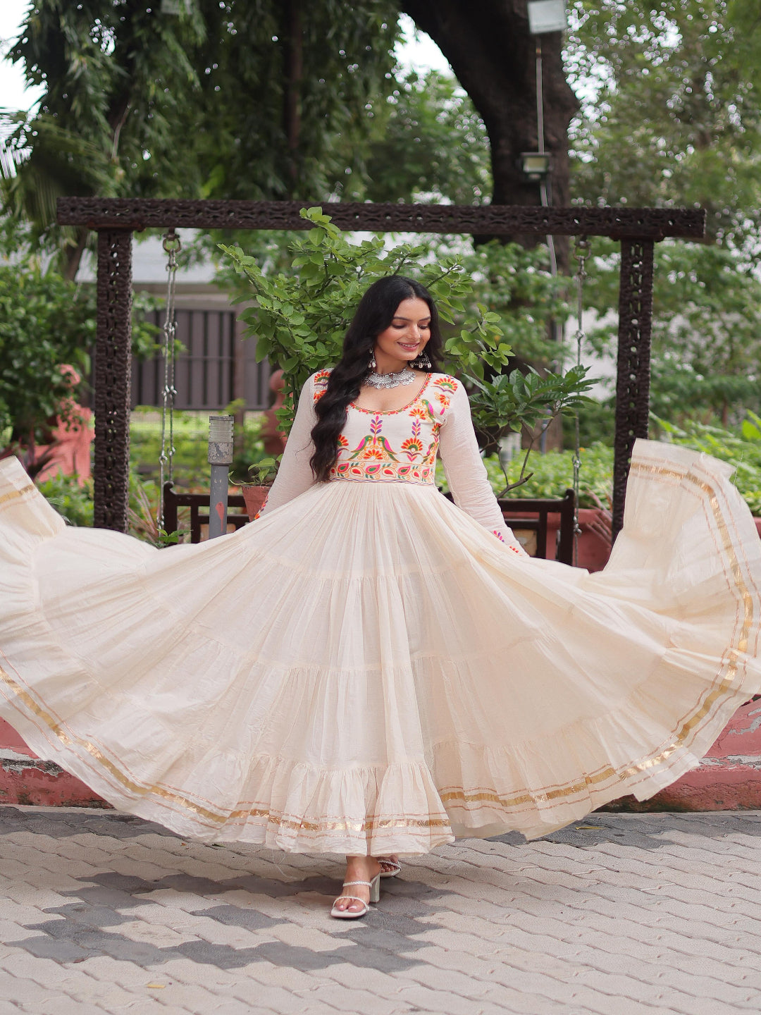 Woman in a traditional outfit with a floral top and beige skirt, standing outdoors.
