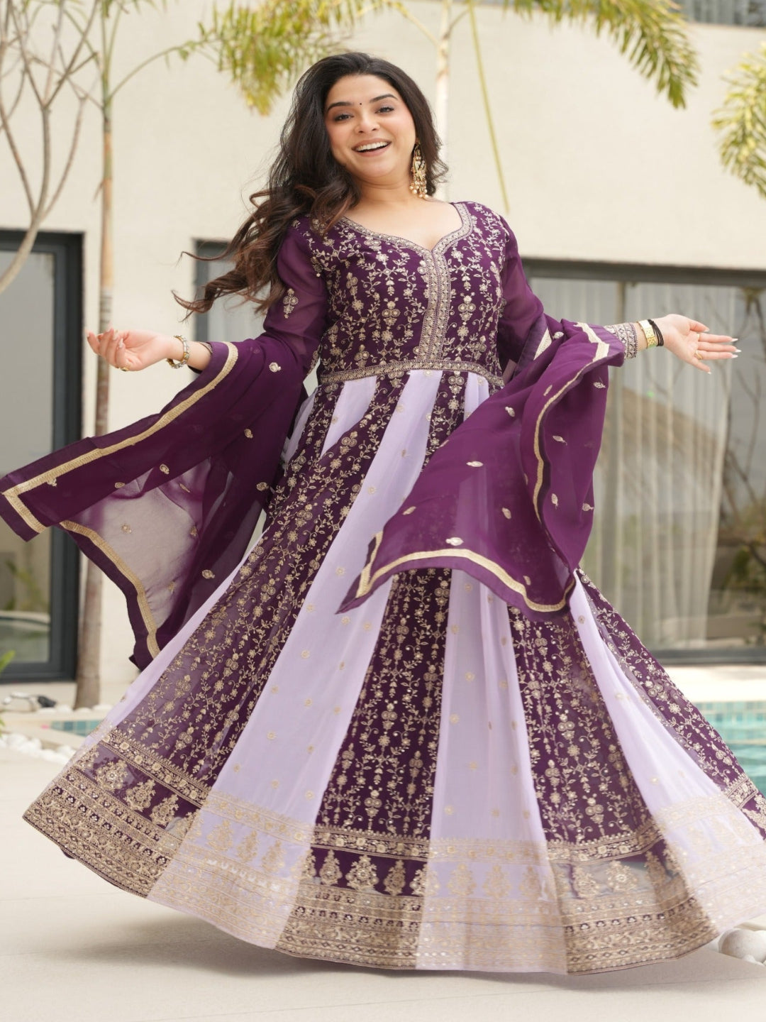 Woman in a purple and white traditional outfit standing outdoors near a pool.