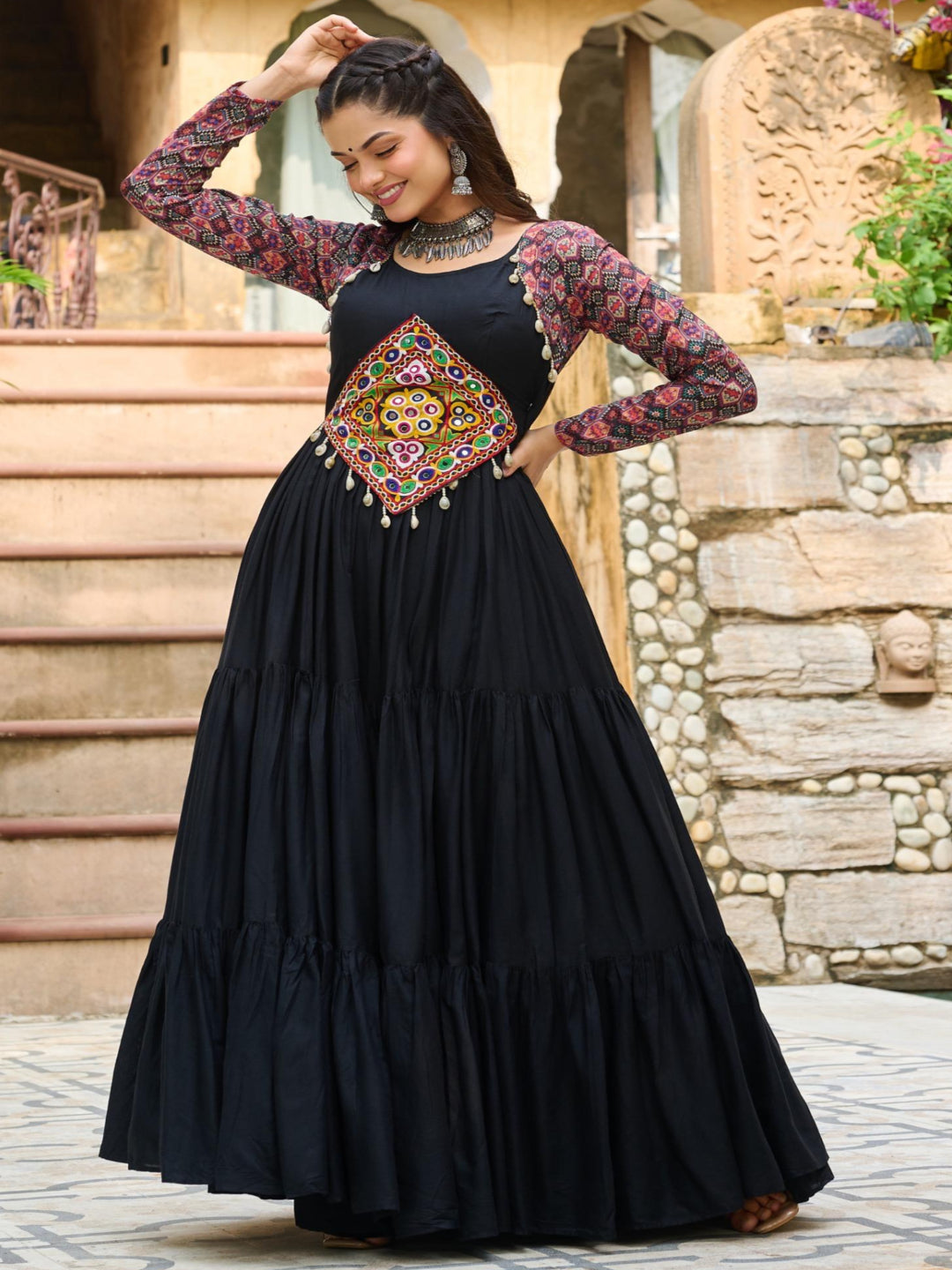Woman in a black dress with floral sleeves and a colorful belt standing outdoors.