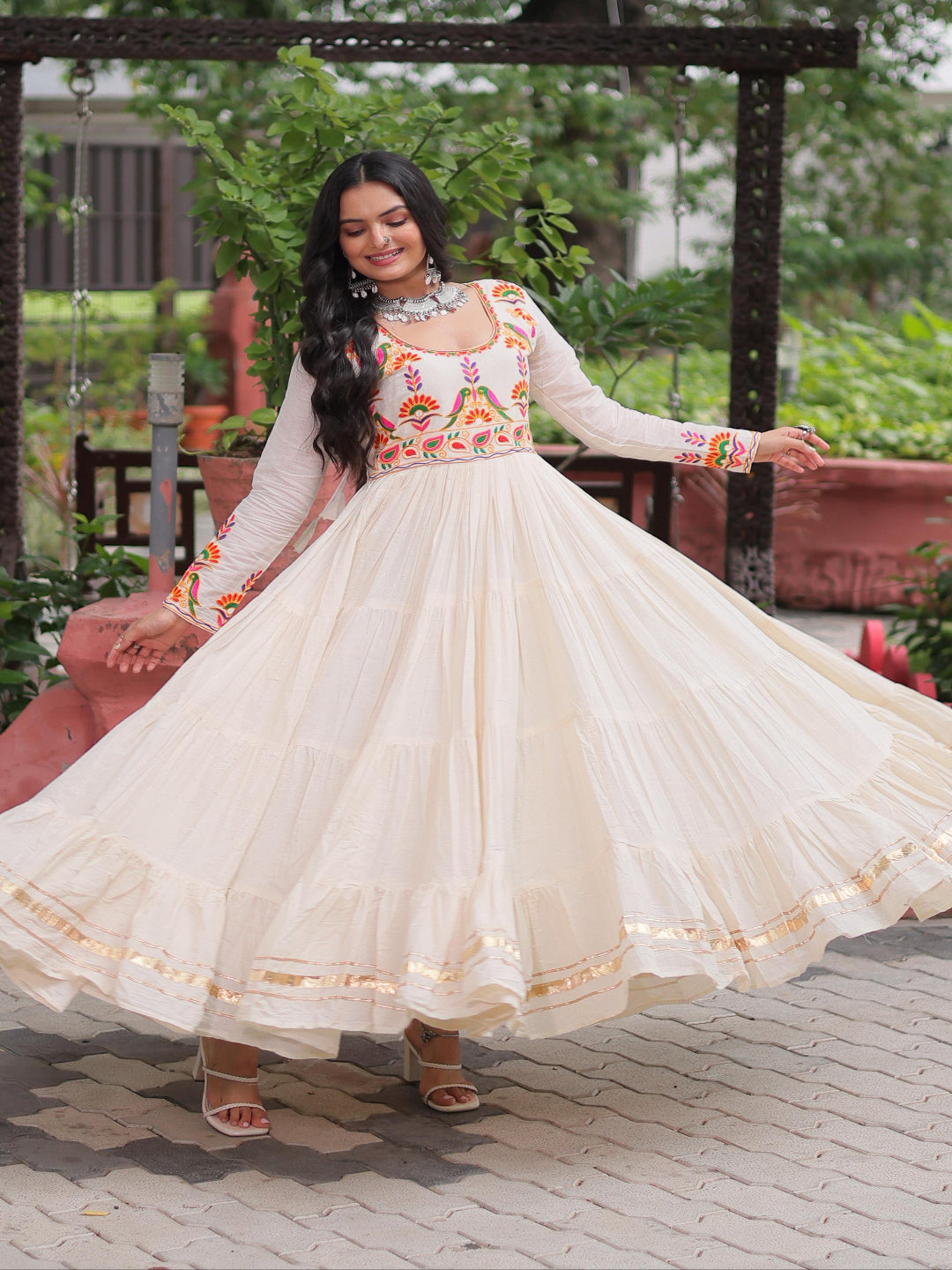 Woman in a traditional outfit with a colorful top and white skirt, standing outdoors.