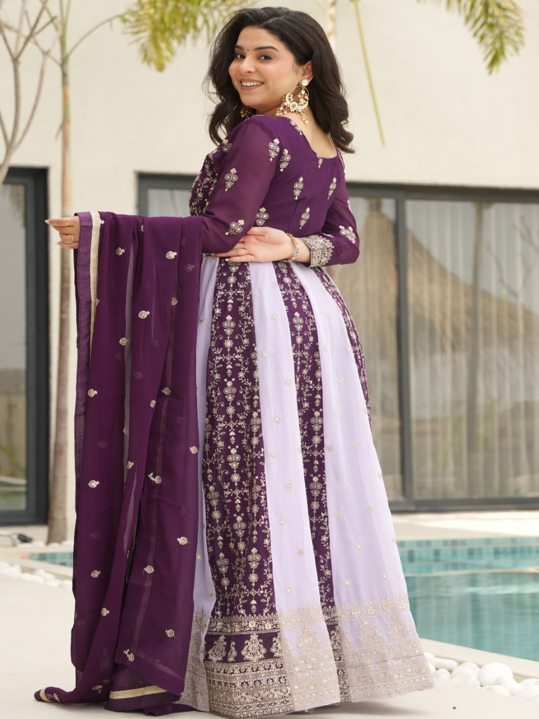 Woman in a purple traditional outfit standing by a pool with a building and trees in the background