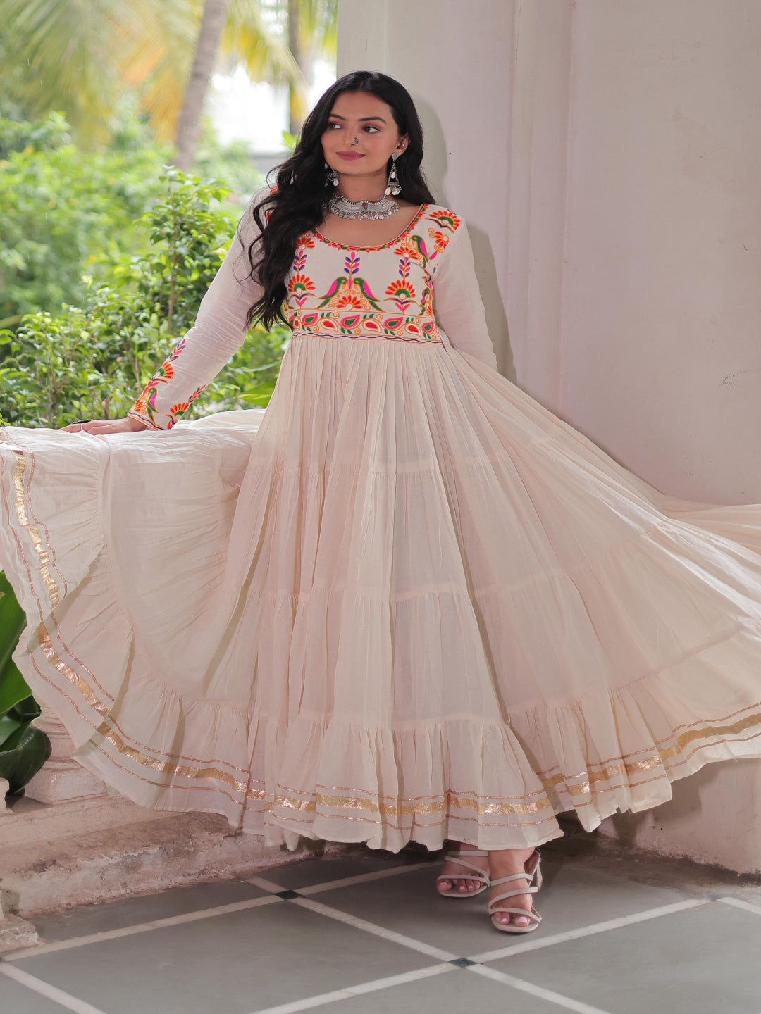 Woman in a traditional outfit standing on a balcony with greenery in the background