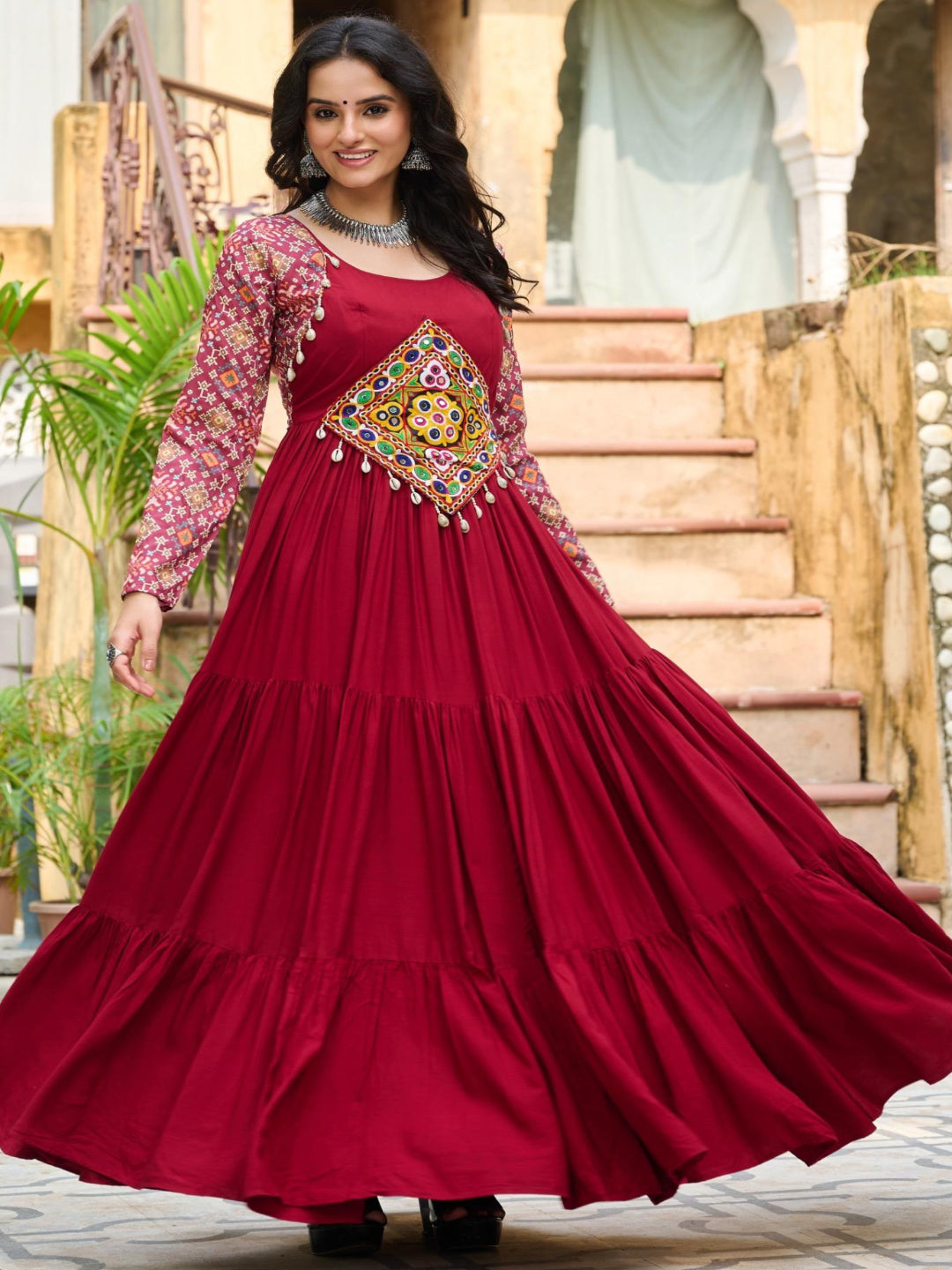 Woman in a red traditional dress with intricate patterns standing in front of a decorative archway.