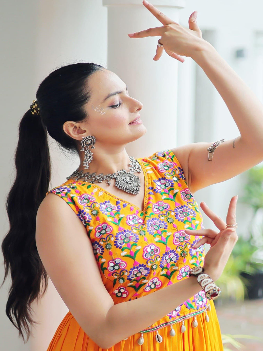 Woman in a colorful traditional outfit with floral patterns, standing indoors.