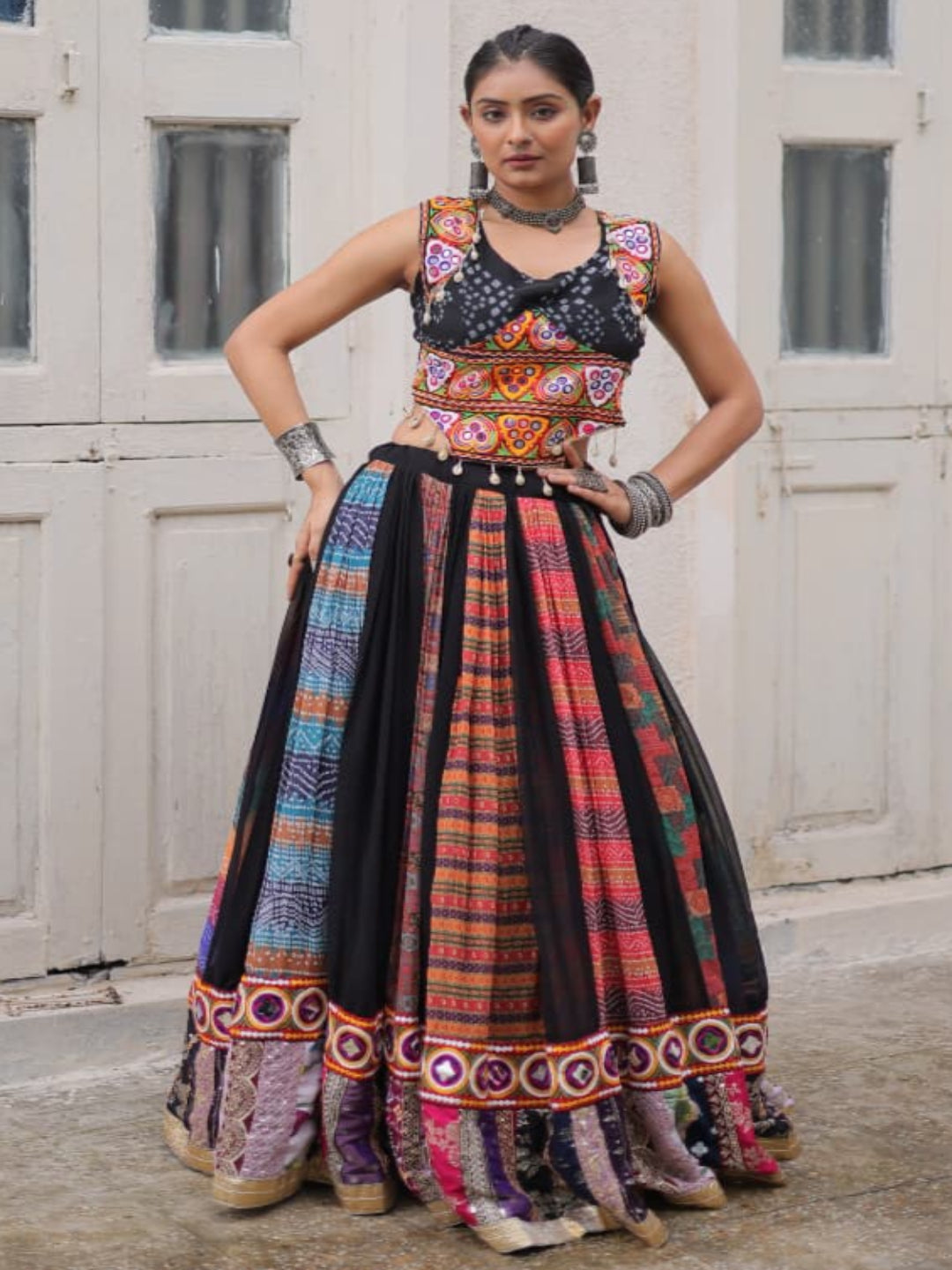 Woman wearing a colorful traditional outfit in front of a white door with arched windows.