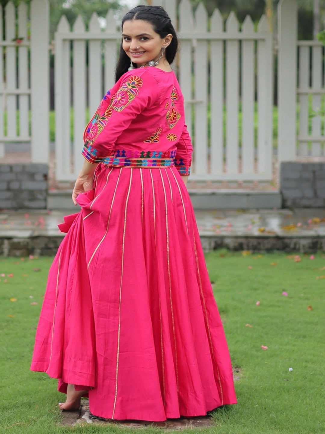 Woman in a bright pink traditional outfit with a colorful blouse standing in a garden.