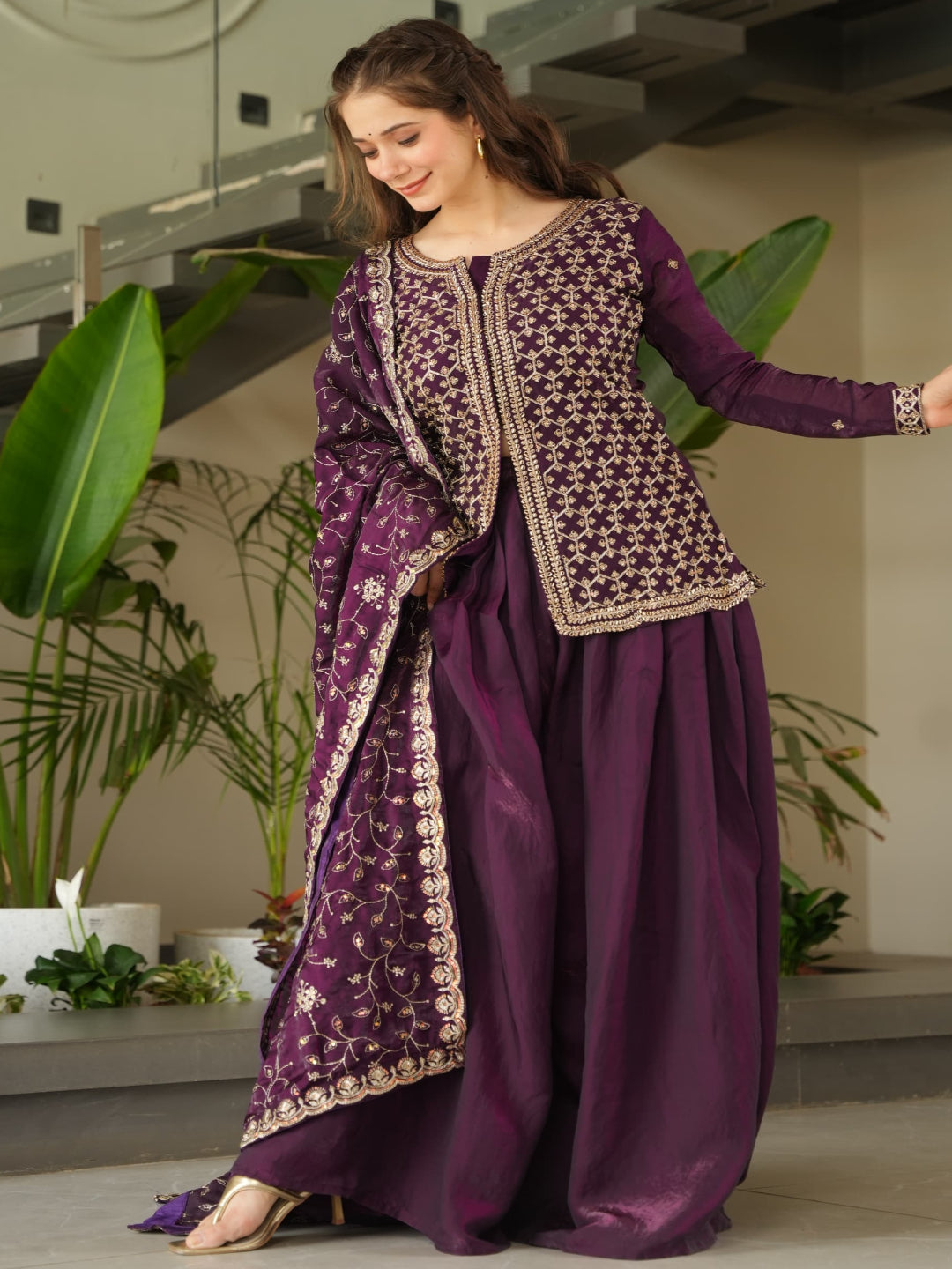 Woman in a purple traditional outfit standing in a modern indoor setting with plants.