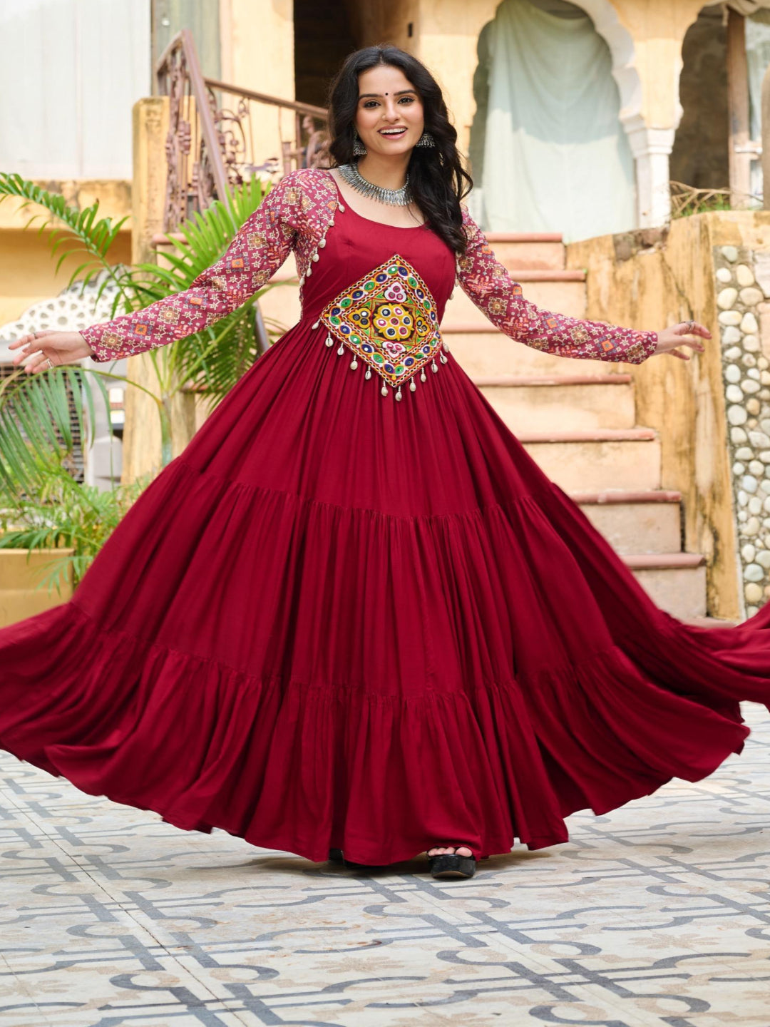 Woman in a red traditional dress with intricate patterns standing in front of an architectural background.