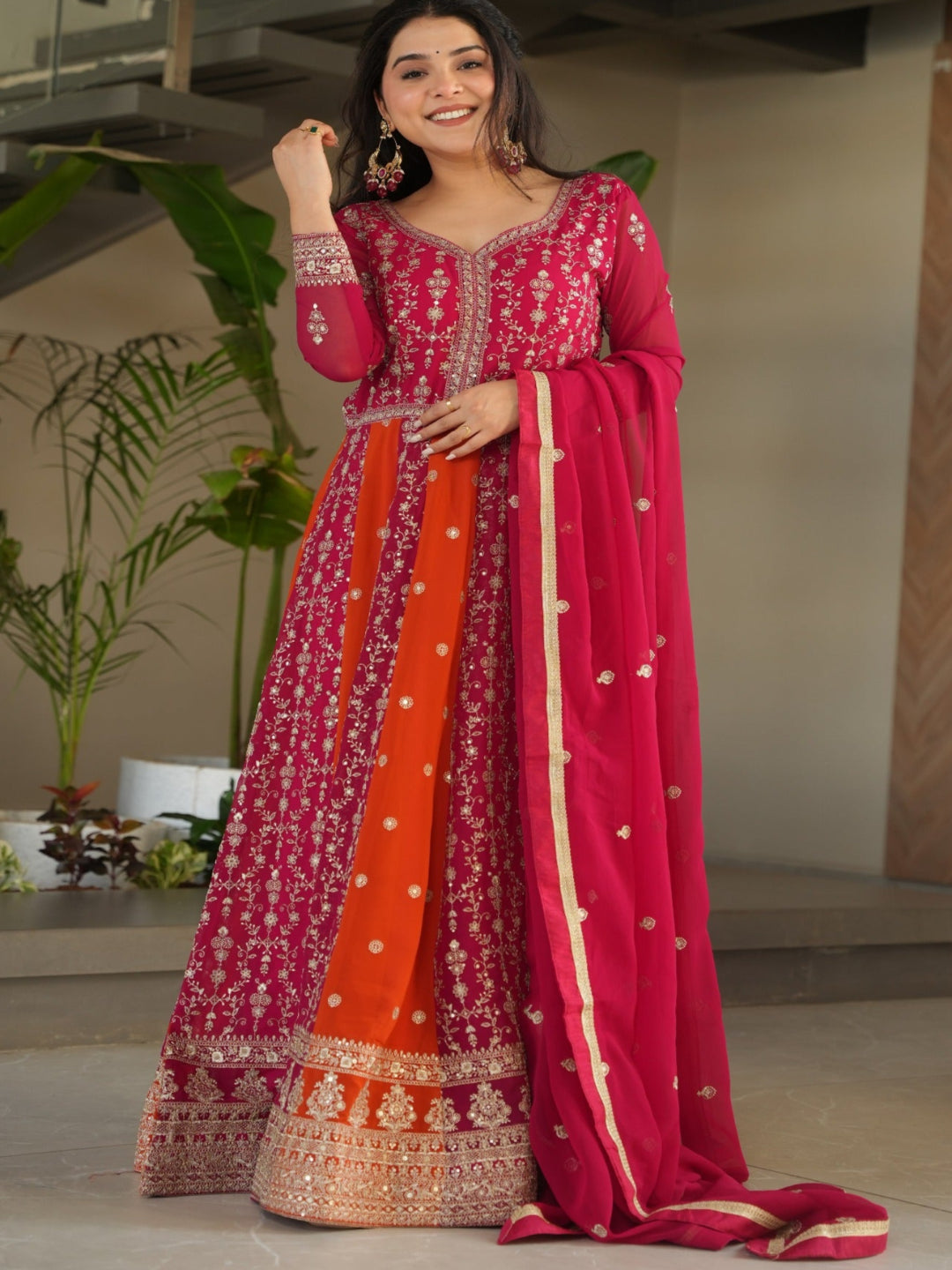 Woman in a vibrant traditional outfit with a pink and orange design indoors.