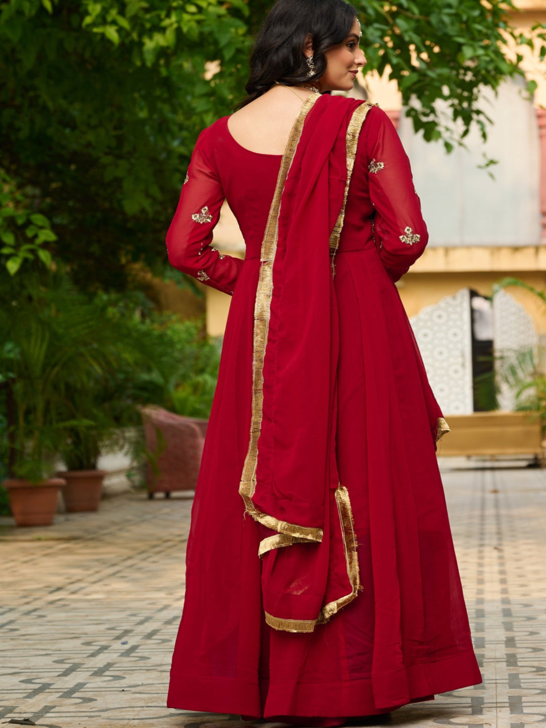Woman in a red traditional outfit with gold details standing outdoors.