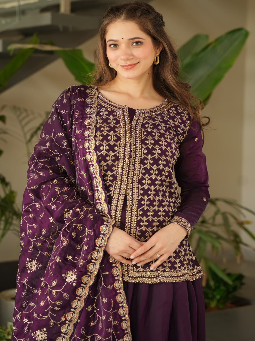Woman wearing a purple traditional outfit with gold embroidery indoors.
