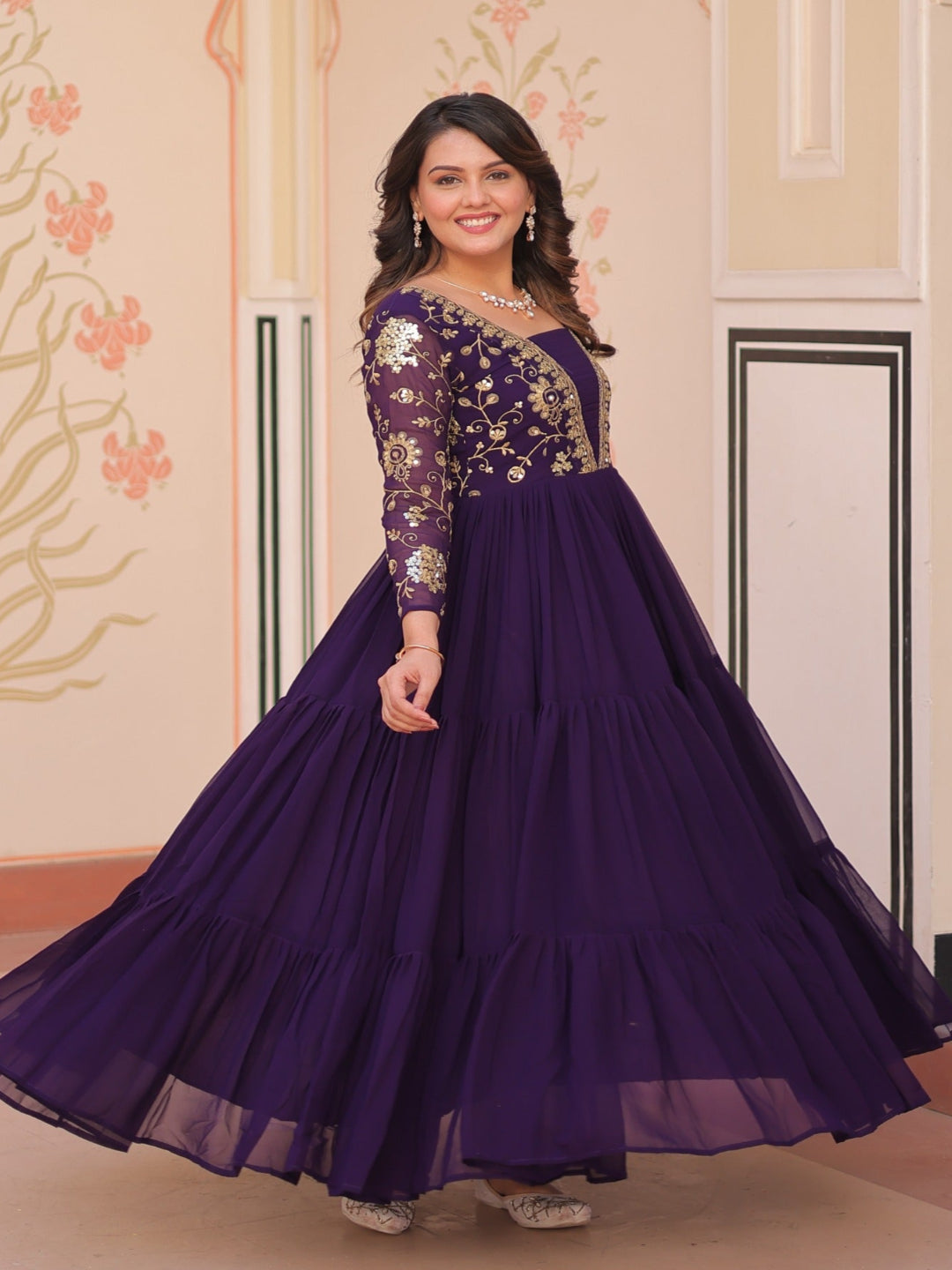 Woman in a purple gown with floral patterns standing in a decorated room.