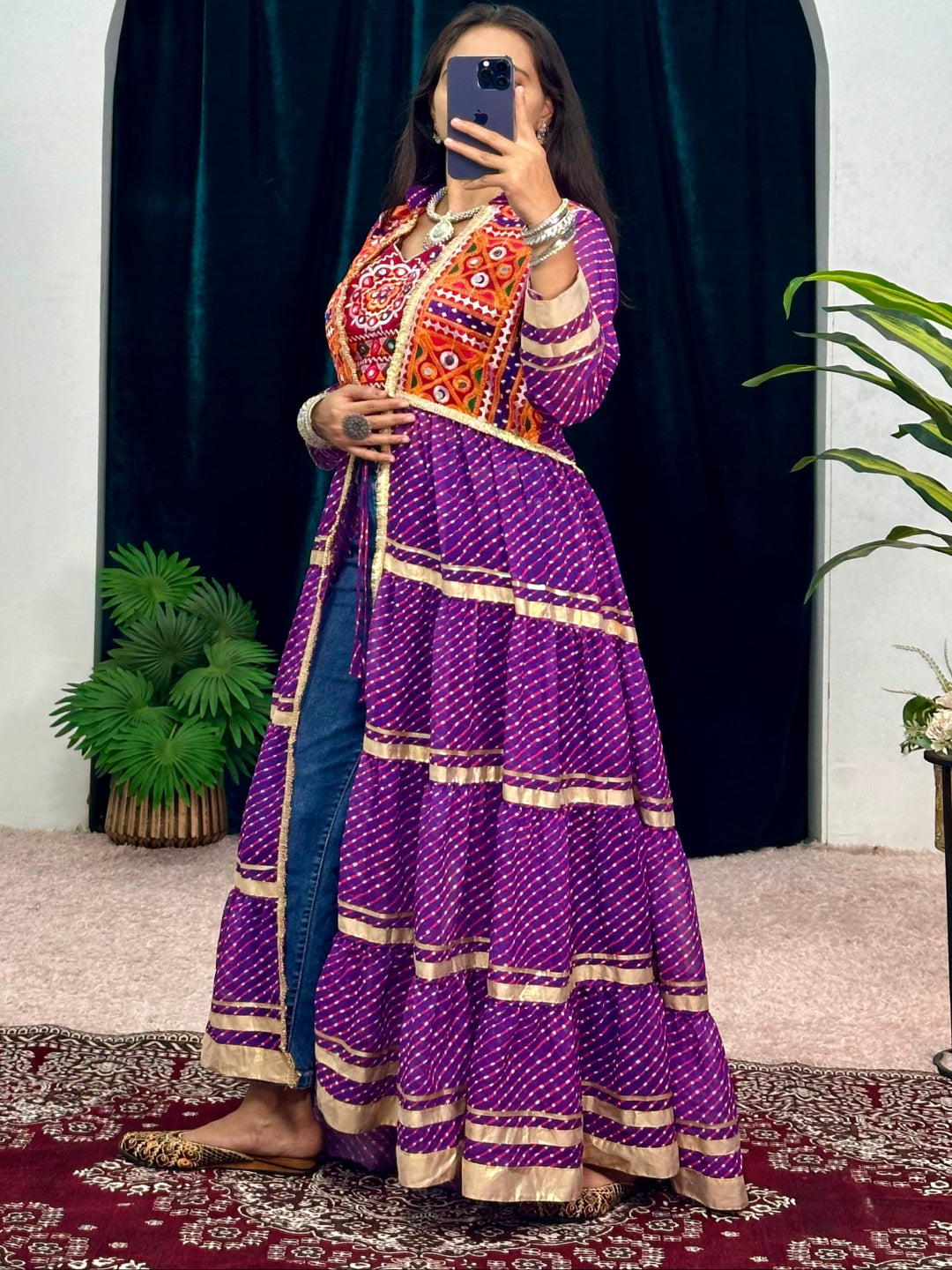Person wearing a colorful traditional outfit taking a mirror selfie in a room with plants and an archway.