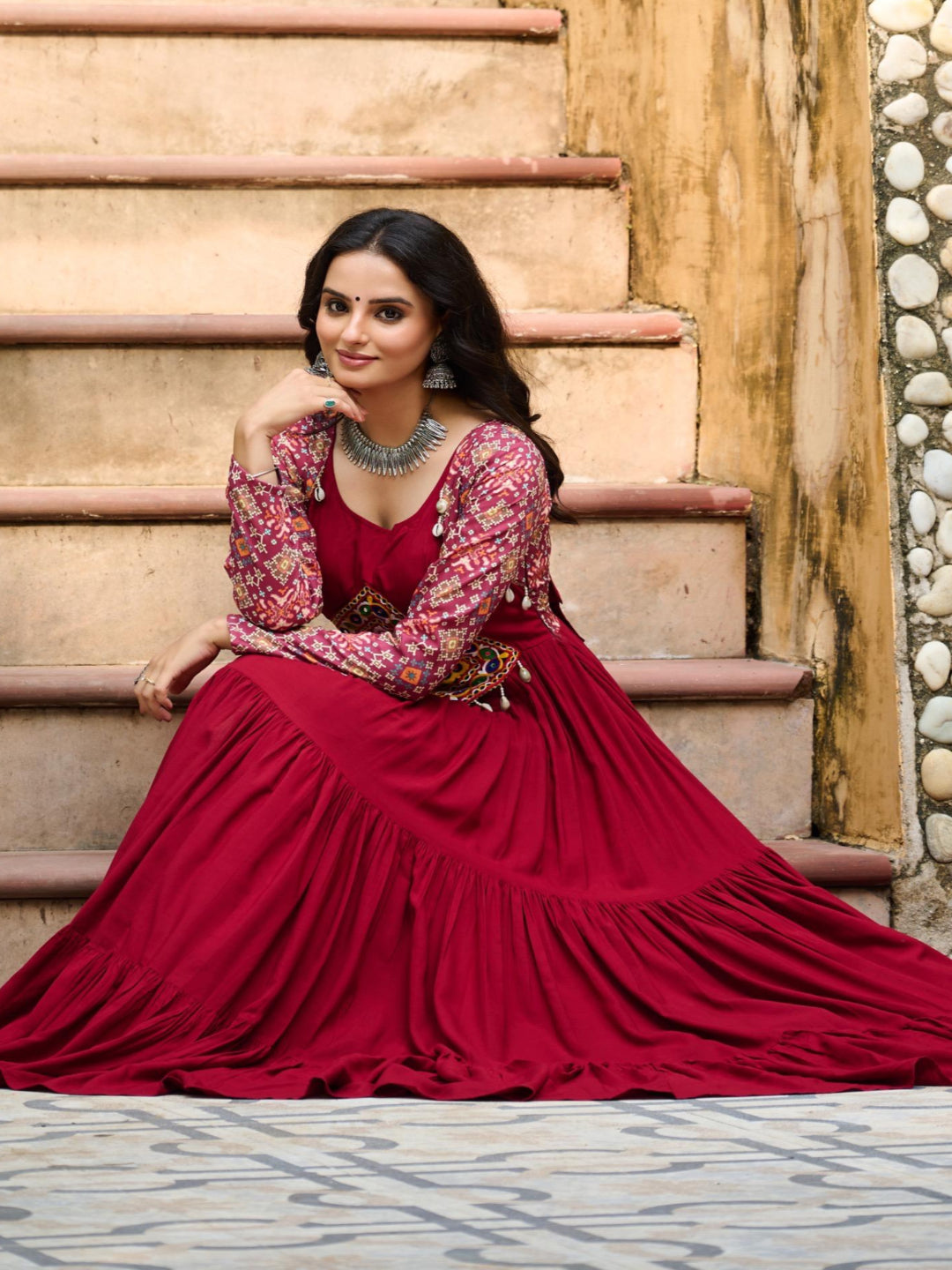Woman in a red traditional outfit sitting on stone steps.
