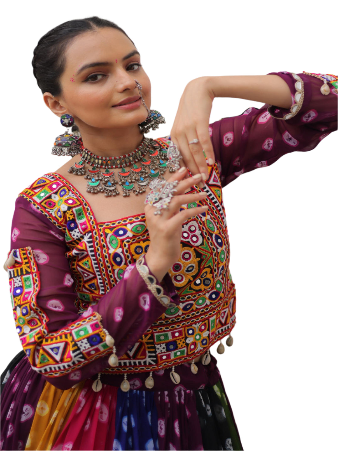 Woman in traditional colorful outfit with jewelry, standing against a light-colored wall.