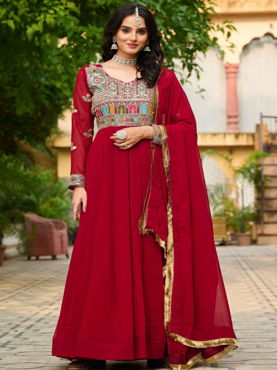 Woman in a red traditional outfit with embroidery standing outdoors.