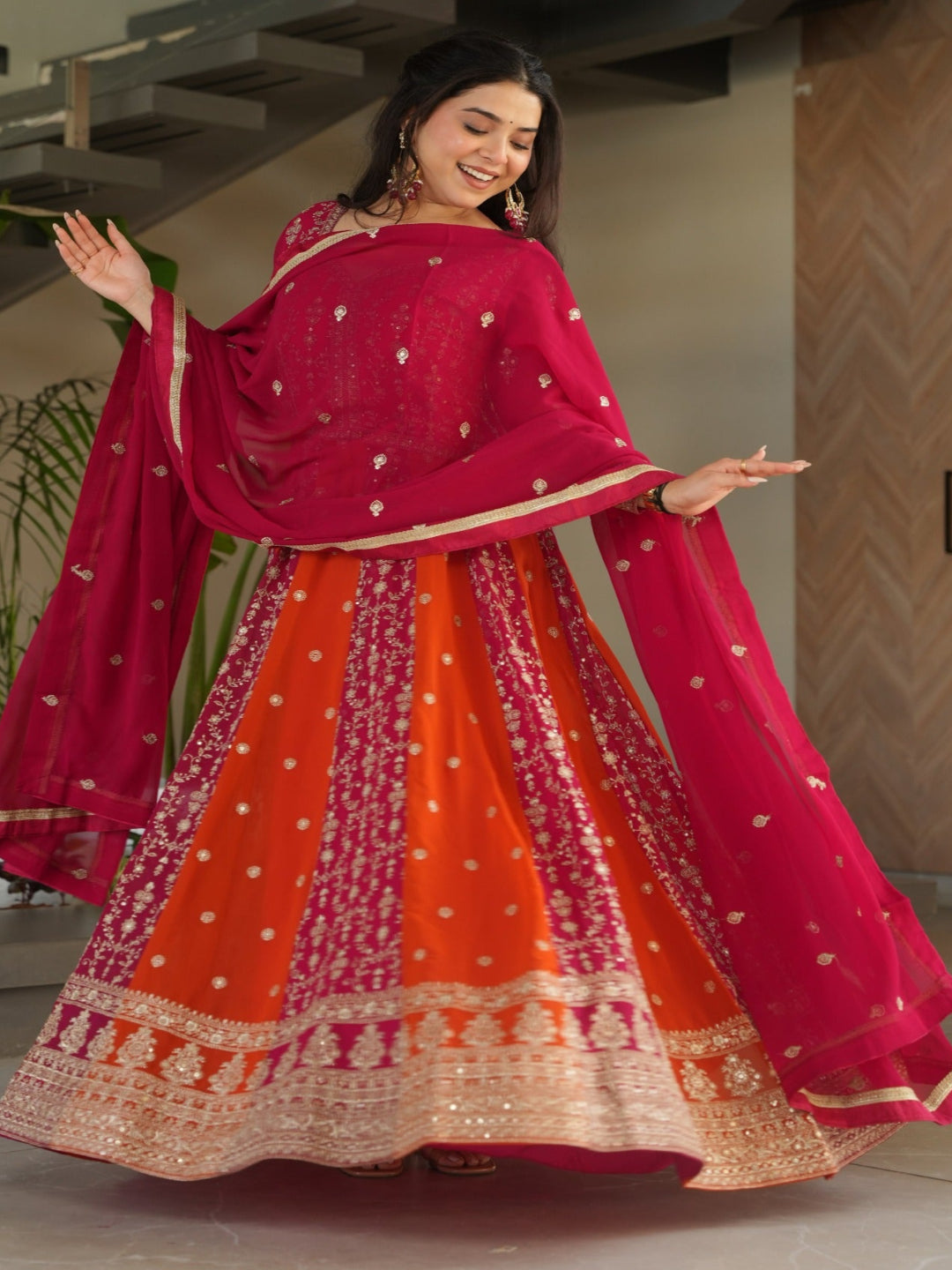 Woman in a vibrant red and orange traditional outfit standing indoors.