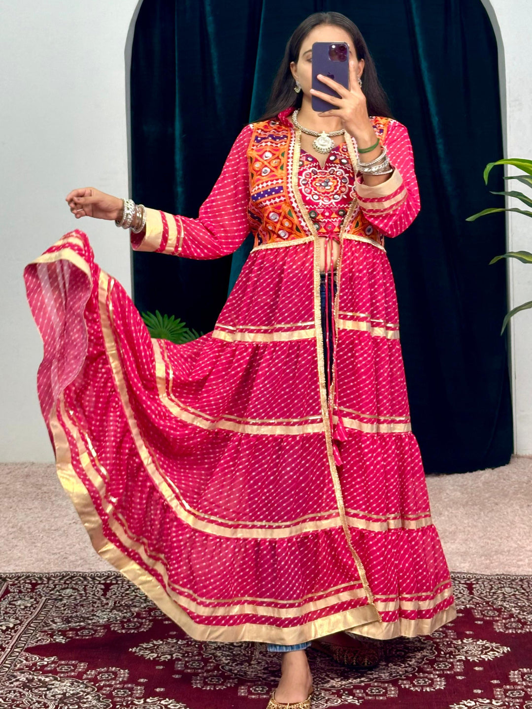 Person wearing a vibrant pink traditional outfit with intricate patterns, standing in front of an archway.