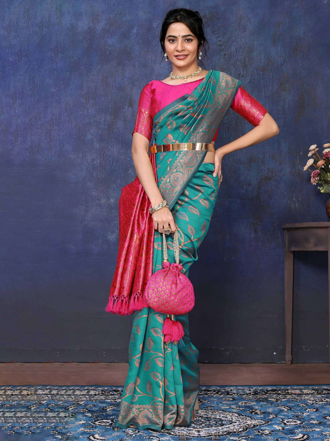 Woman wearing a green saree with pink blouse against a blue textured wall.
