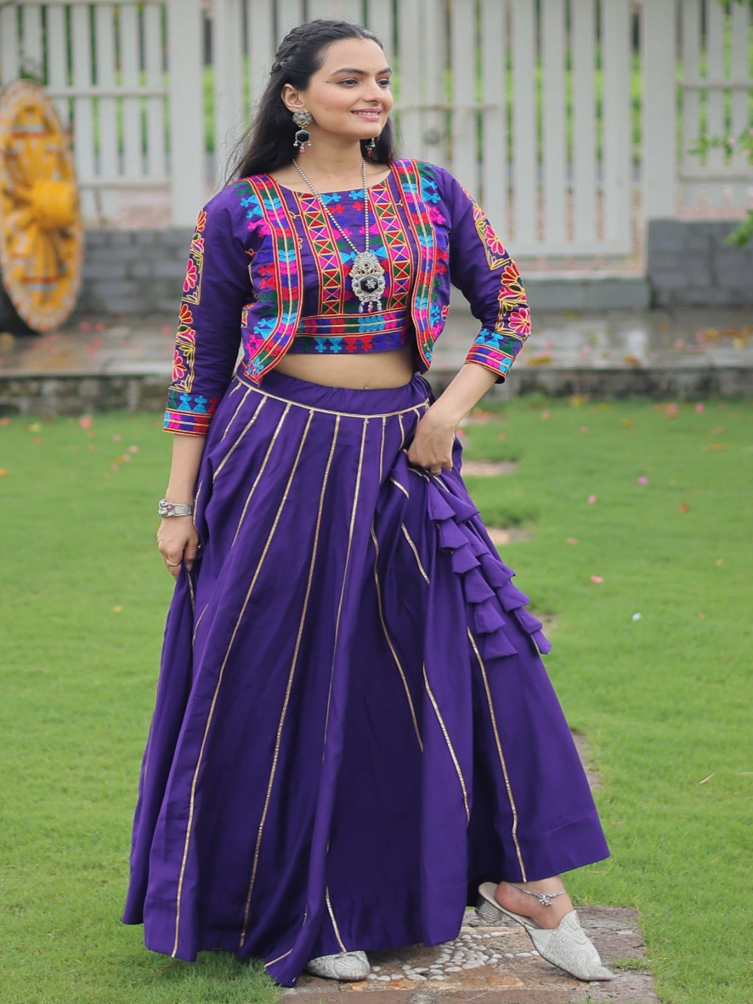 Woman in traditional outfit standing on grass with a decorative background