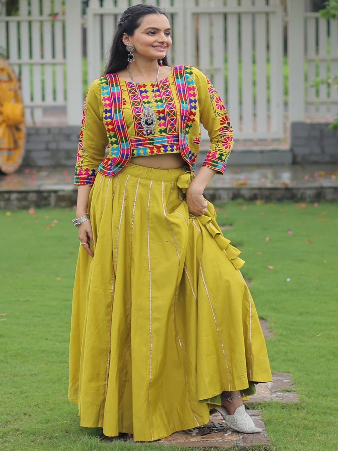 Woman in colorful top and yellow skirt standing in a garden with floral decorations.