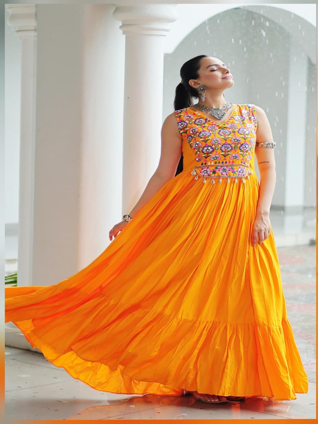 Two women wearing colorful embroidered dresses, one orange and one red, in an outdoor setting.
