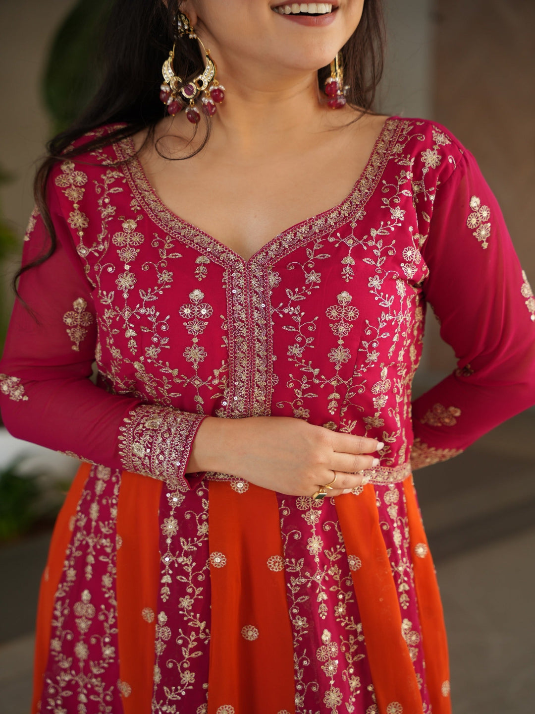 Woman wearing a pink and red traditional outfit with intricate embroidery.