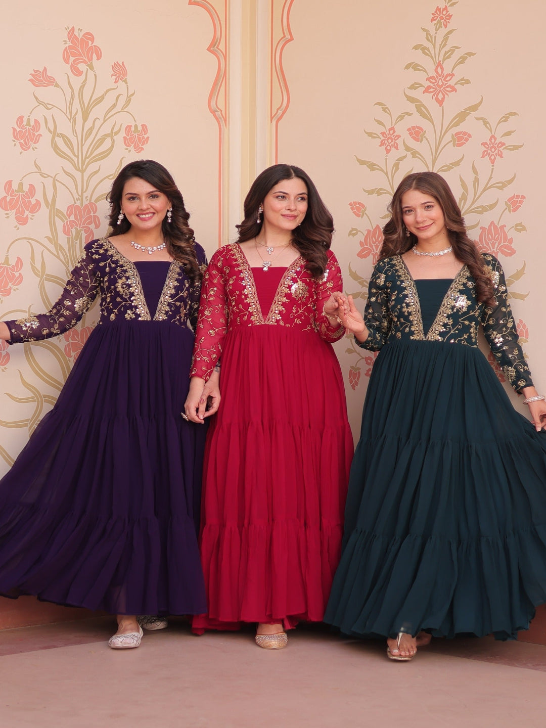 Three women in colorful traditional dresses standing against a decorative wall.