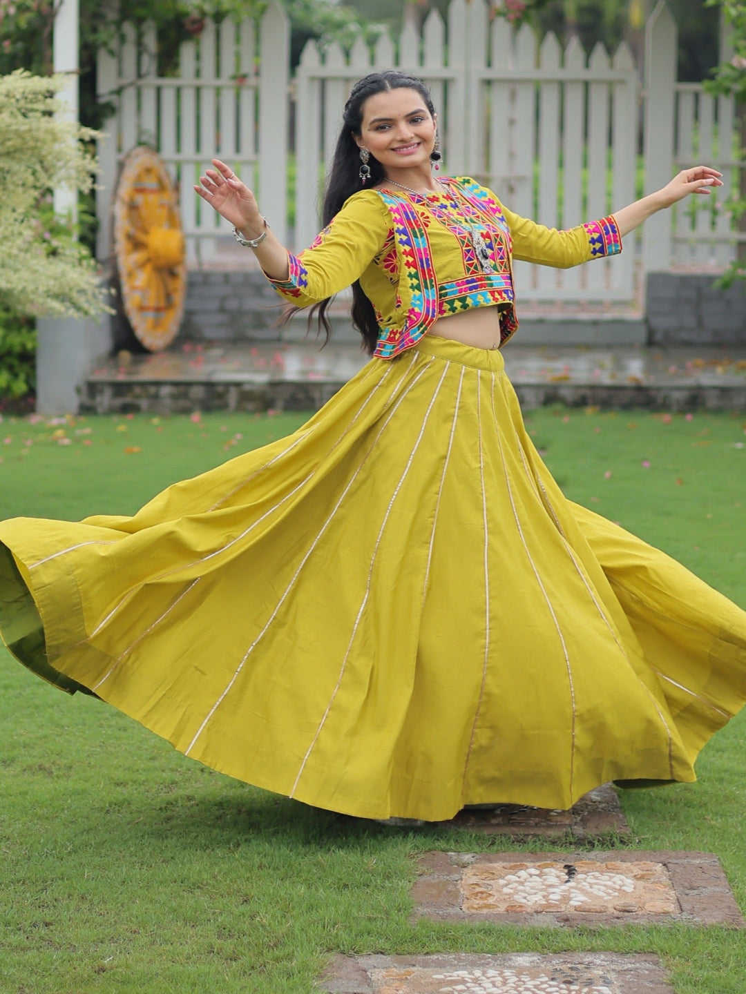 Woman in a yellow traditional outfit with colorful blouse dancing in a garden.