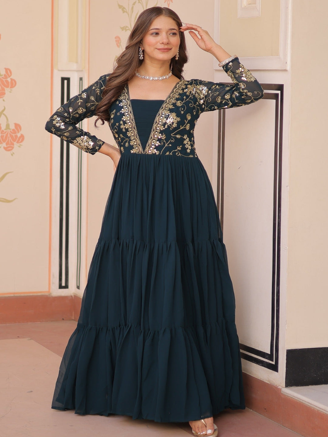 Woman in a dark blue dress with floral embroidery standing in an ornate room.