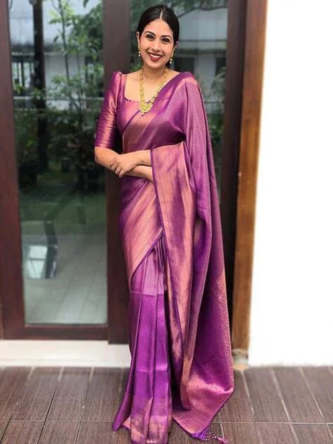 Woman wearing a purple saree with a matching blouse, standing indoors.
