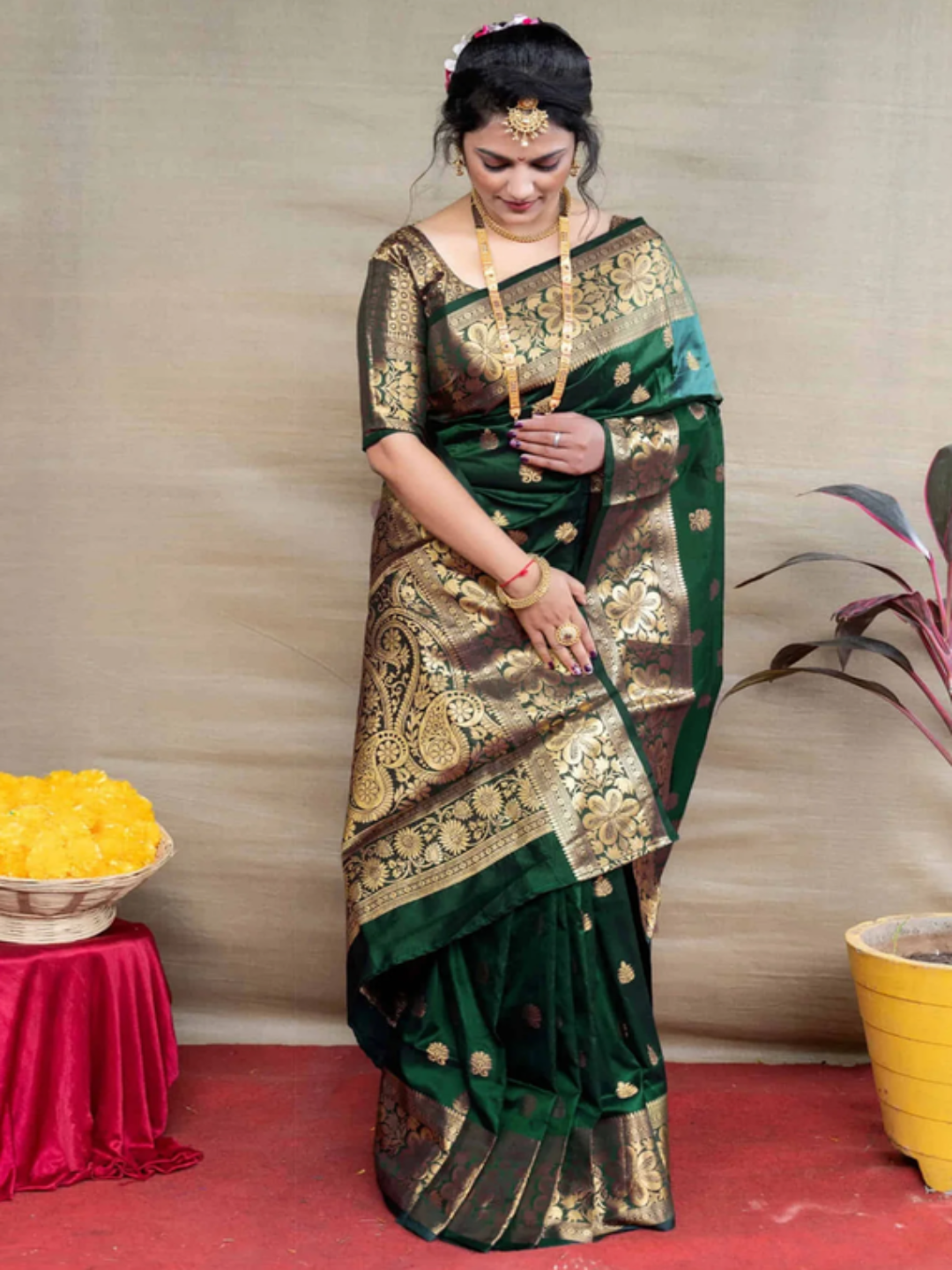Woman in a green and gold saree standing indoors with a neutral background