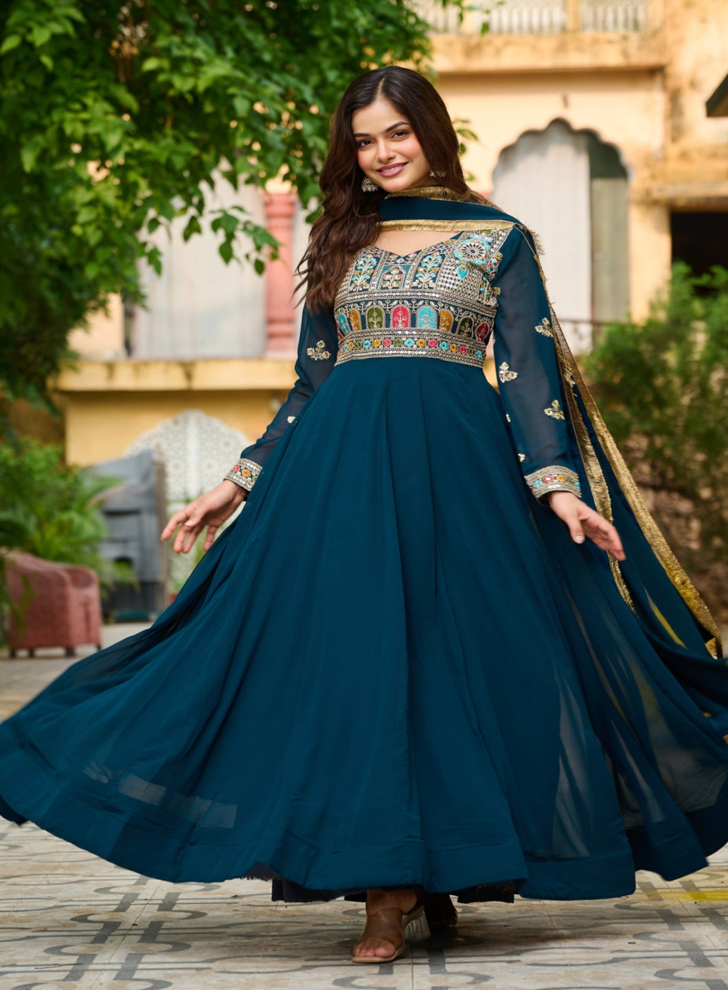 Woman in a traditional blue dress with intricate patterns standing outdoors.