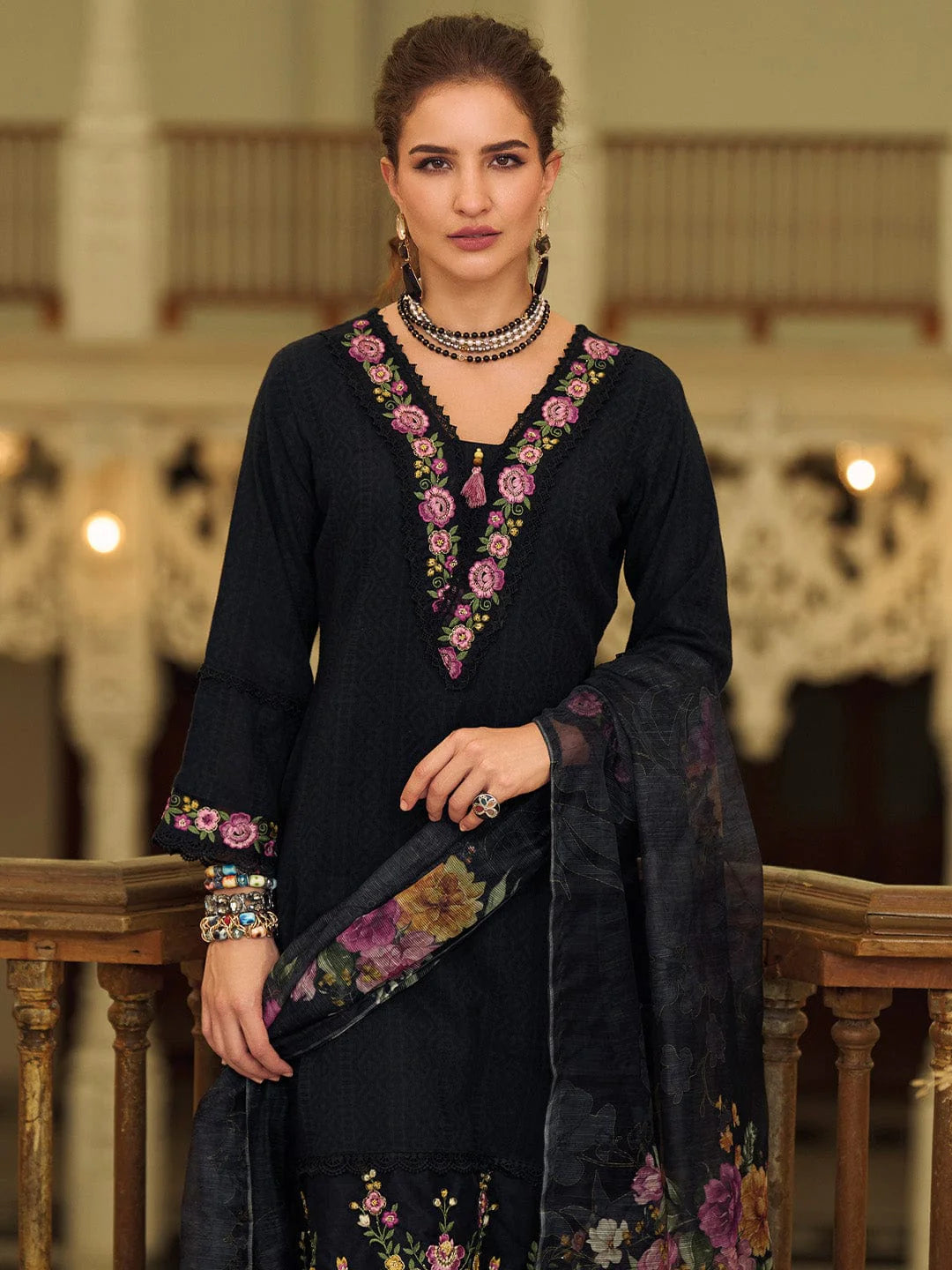 Woman wearing a black embroidered outfit with floral patterns in an elegant indoor setting.