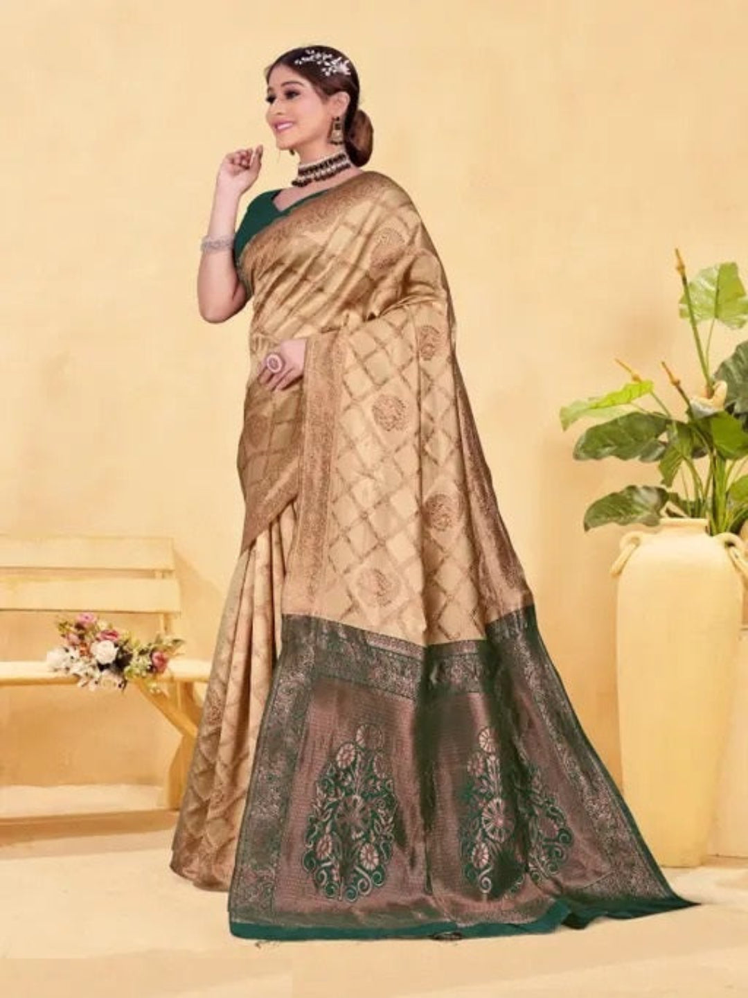 Woman wearing a beige and brown saree with a decorative pattern, standing against a light yellow background.