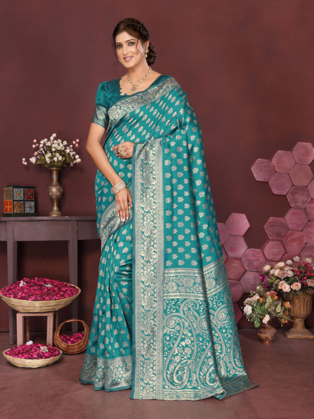 Woman wearing a teal saree with a patterned border in a decorated room.