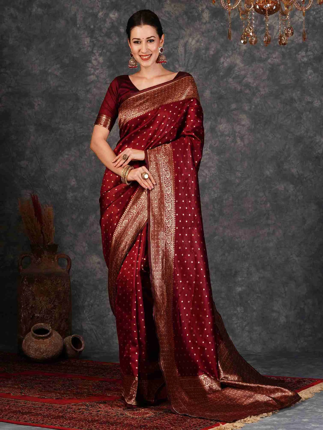 Woman wearing a red saree with gold patterns against a dark background