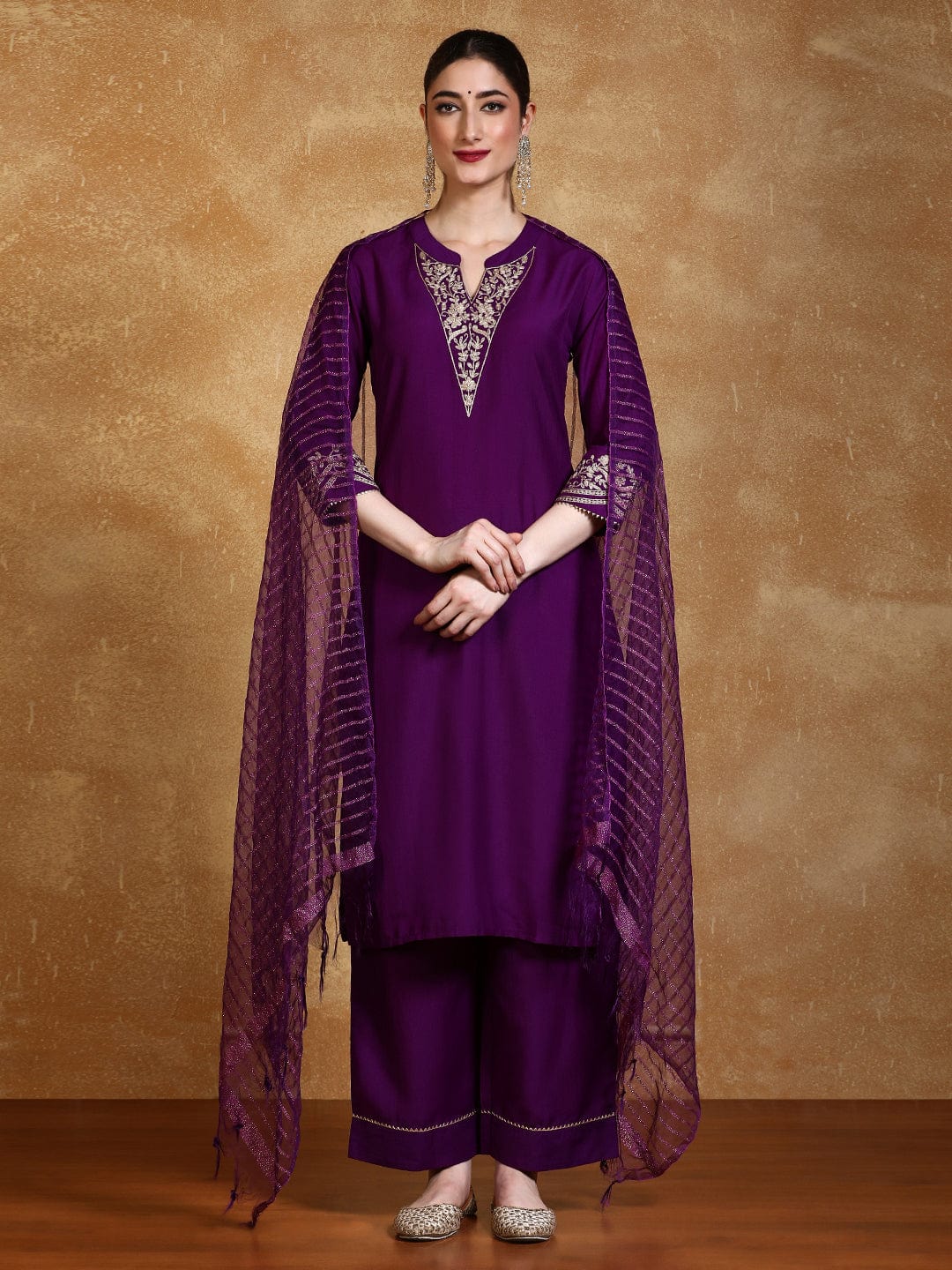 Woman wearing a purple traditional outfit with a matching dupatta against a brown background