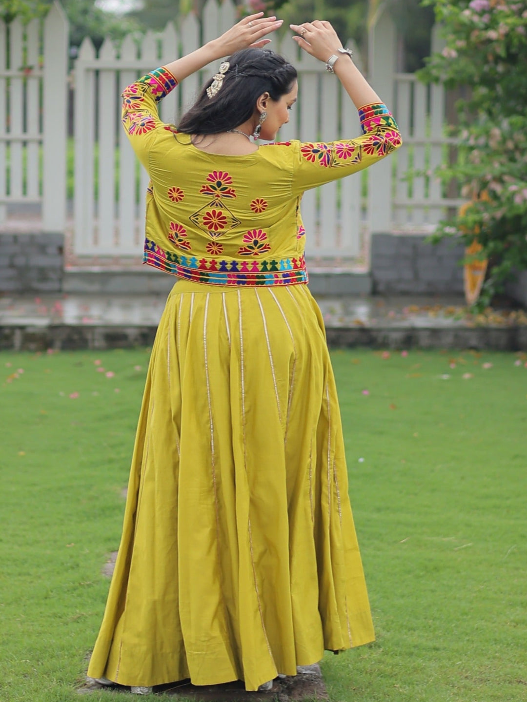 Woman in a yellow traditional outfit with floral embroidery standing in a garden.