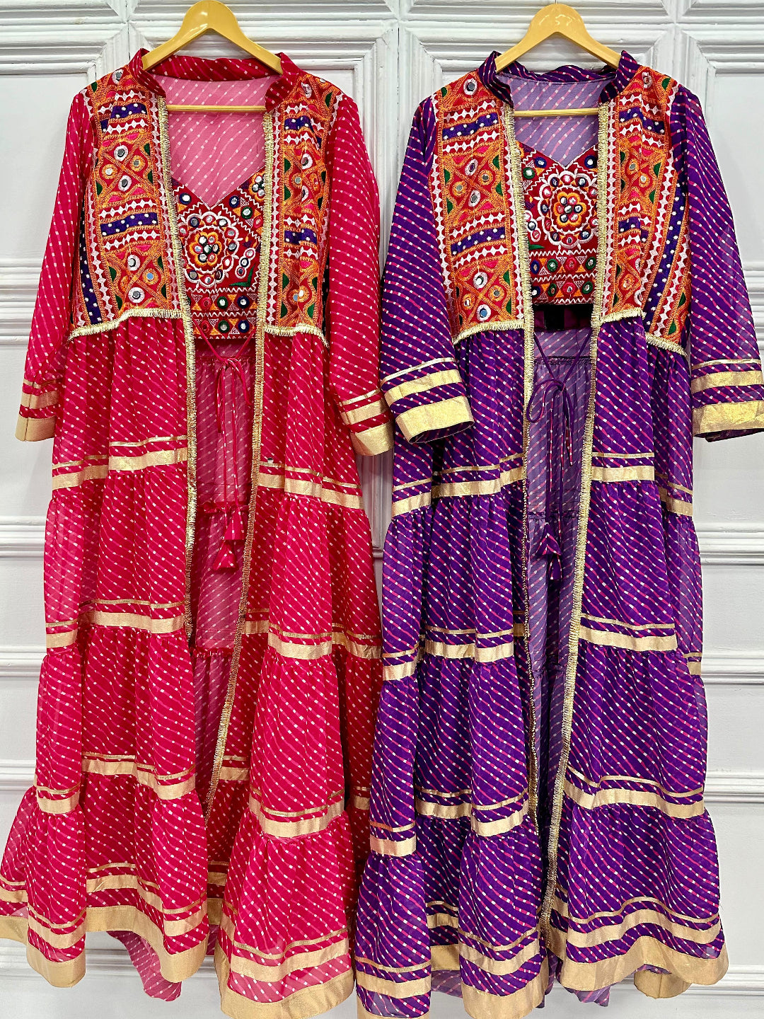 Two traditional outfits, one pink and one purple, with intricate patterns on a white background.