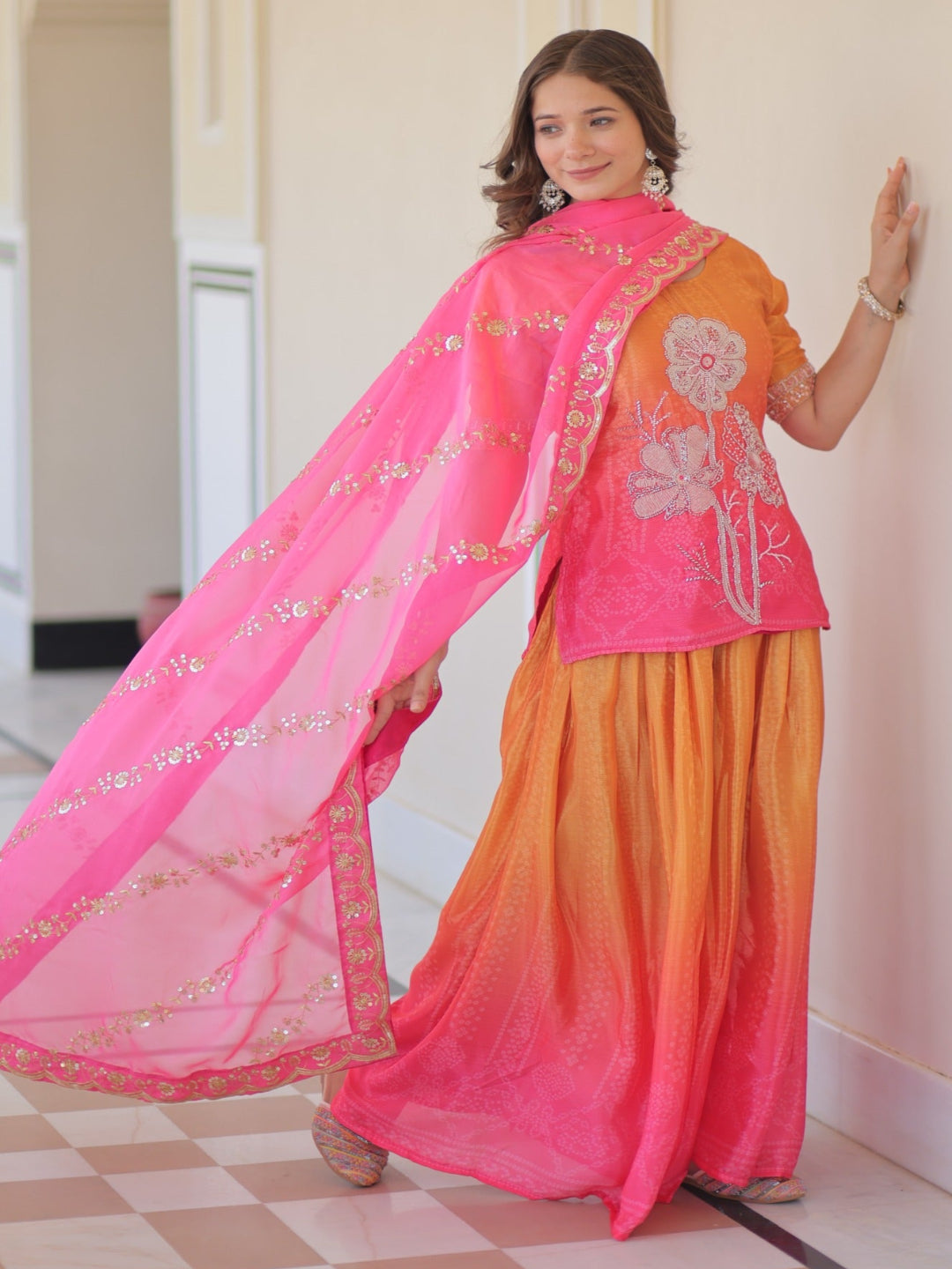 Woman wearing a traditional outfit with a pink and orange dupatta in an indoor setting.