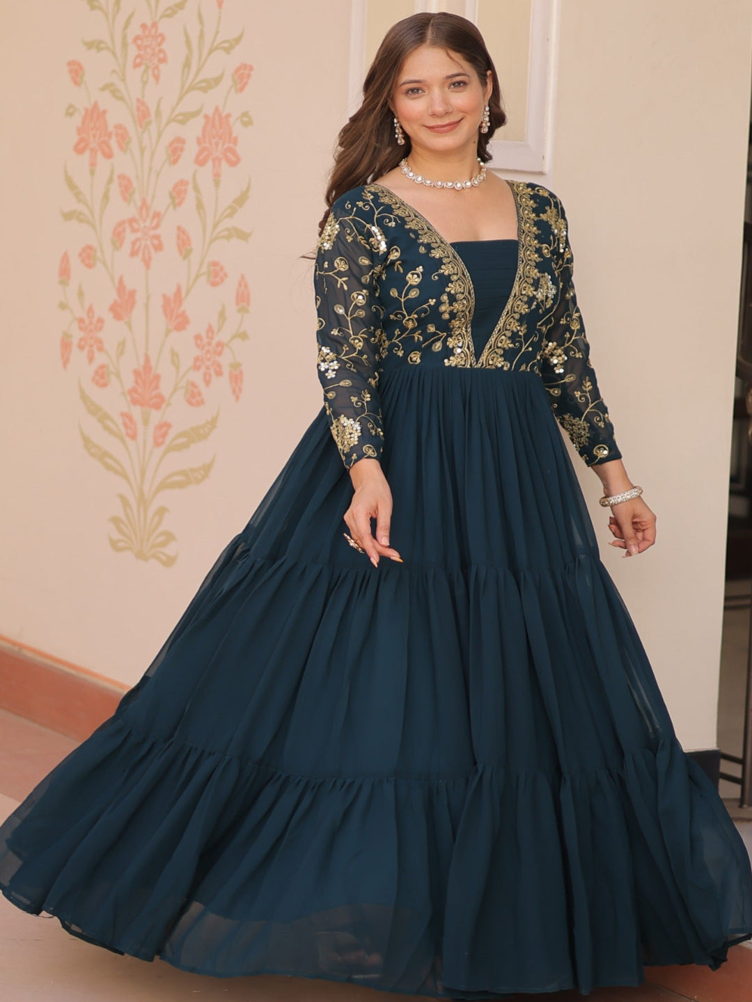 Woman in a dark blue gown with floral embroidery standing indoors.