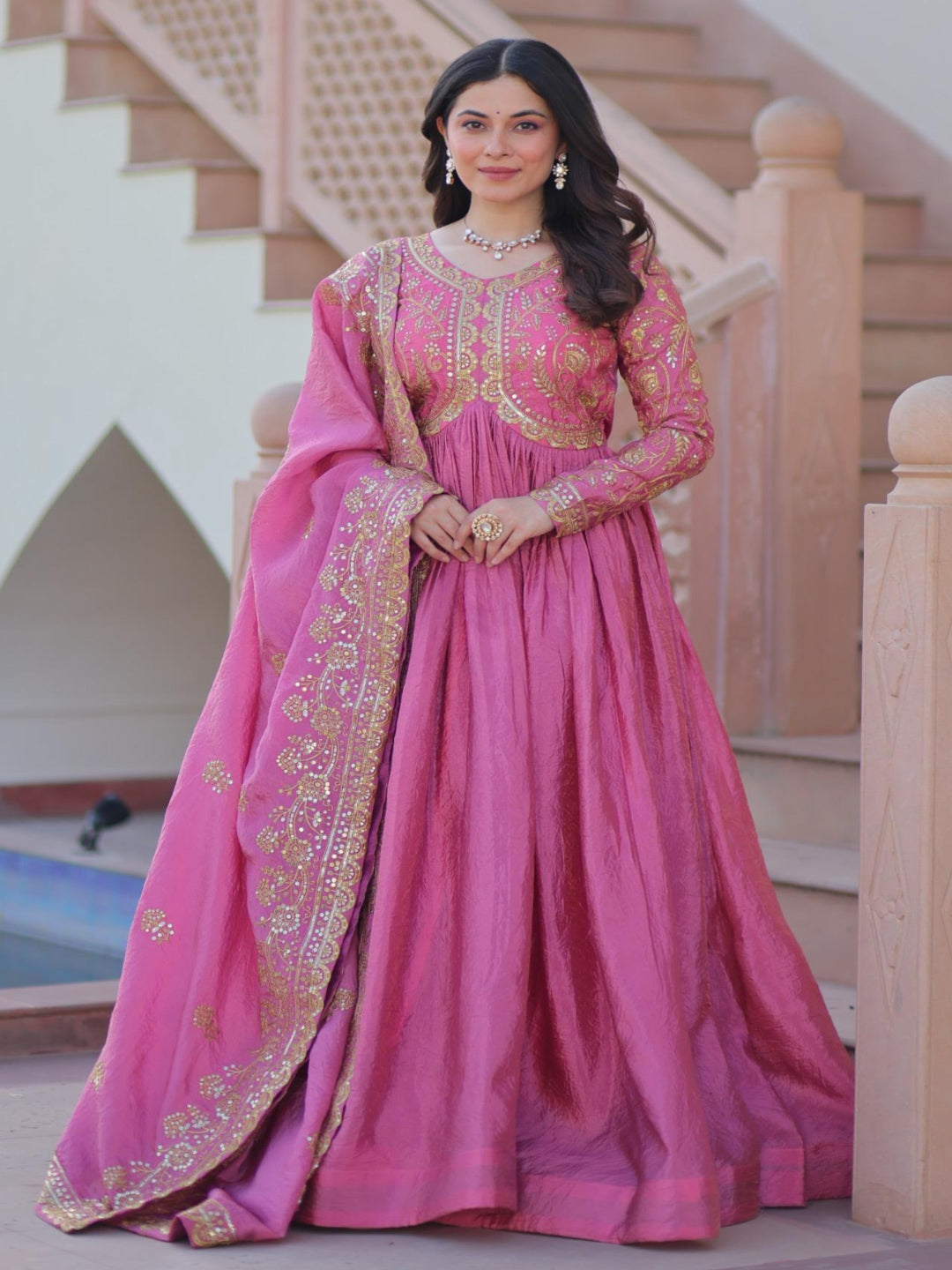 Woman in a pink traditional outfit standing in front of a staircase.
