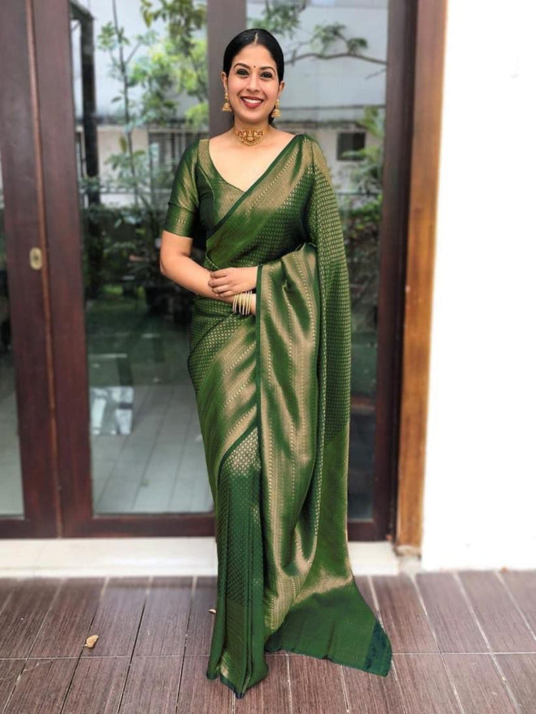 Woman wearing a green saree standing indoors with a blurred background