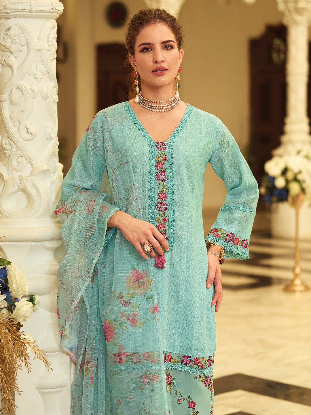 Woman wearing a light blue embroidered dress in an elegant indoor setting.