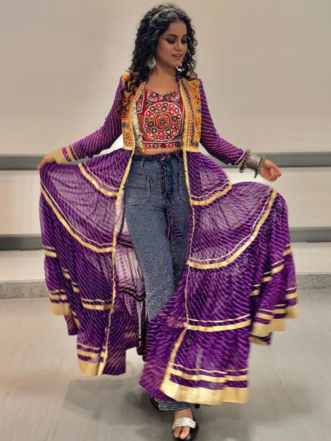 Woman wearing a vibrant traditional outfit with a long purple dress and colorful top.