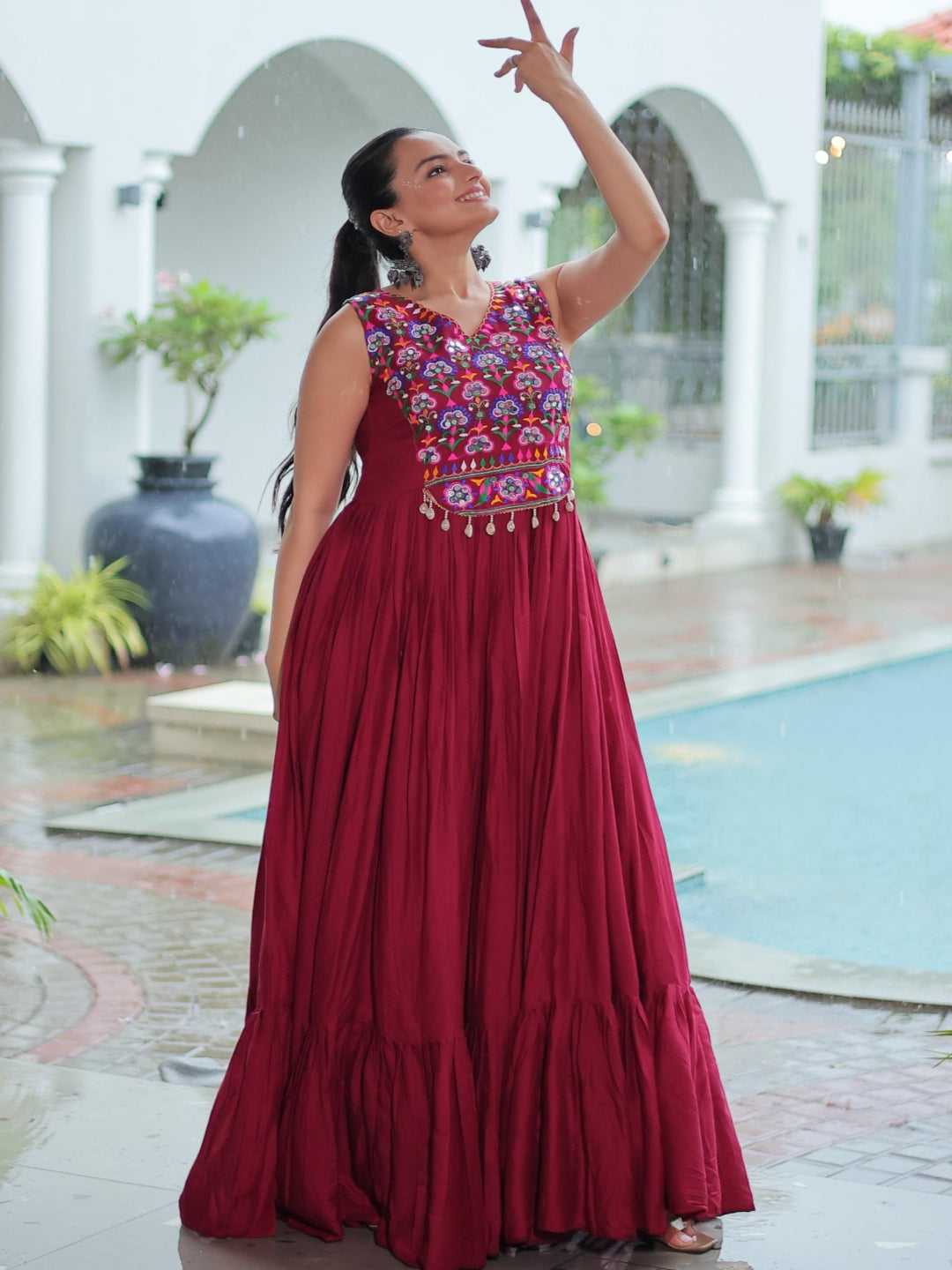 Woman in a red dress with floral patterns standing by a poolside.