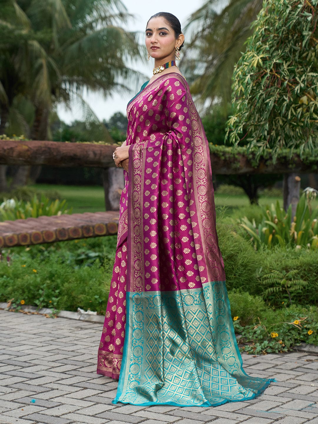 Woman wearing a traditional saree with a pink and green pattern in an outdoor setting.